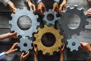 Group of business people joining together silver and golden colored gears on table at workplace top view