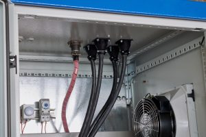 Several power cables of black color are removed through the holes and fixed in the body of the electrical Cabinet. Fan is mounted on the side wall to cool the electrical equipment inside the Cabinet.