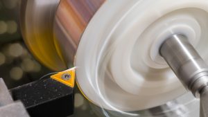 Turning a plastic cylinder with an aluminum surface. Metal cutting tool with wavy swarf. Beautiful motion blur. Bokeh on background