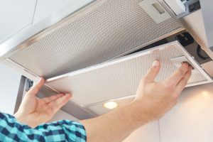 Mans hands removing a filter from cooker hood for cleaning or service. Replacing filter in kitchen hood. Modern kitchen fan.