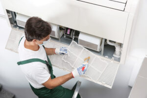 Young male technician cleaning air conditioner indoors