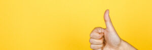 closeup of thumbs up symbol on yellow background.