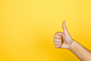 closeup of thumbs up symbol on yellow background.