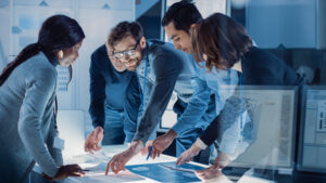 Engineers Meeting in Technology Research Laboratory: Engineers, Scientists and Developers Gathered Around Illuminated Conference Table, Talking and Finding Solution, Inspecting and Analysing Industrial Engine Design.